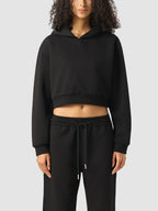 Person wearing a black cropped hoodie and black pants on a white background