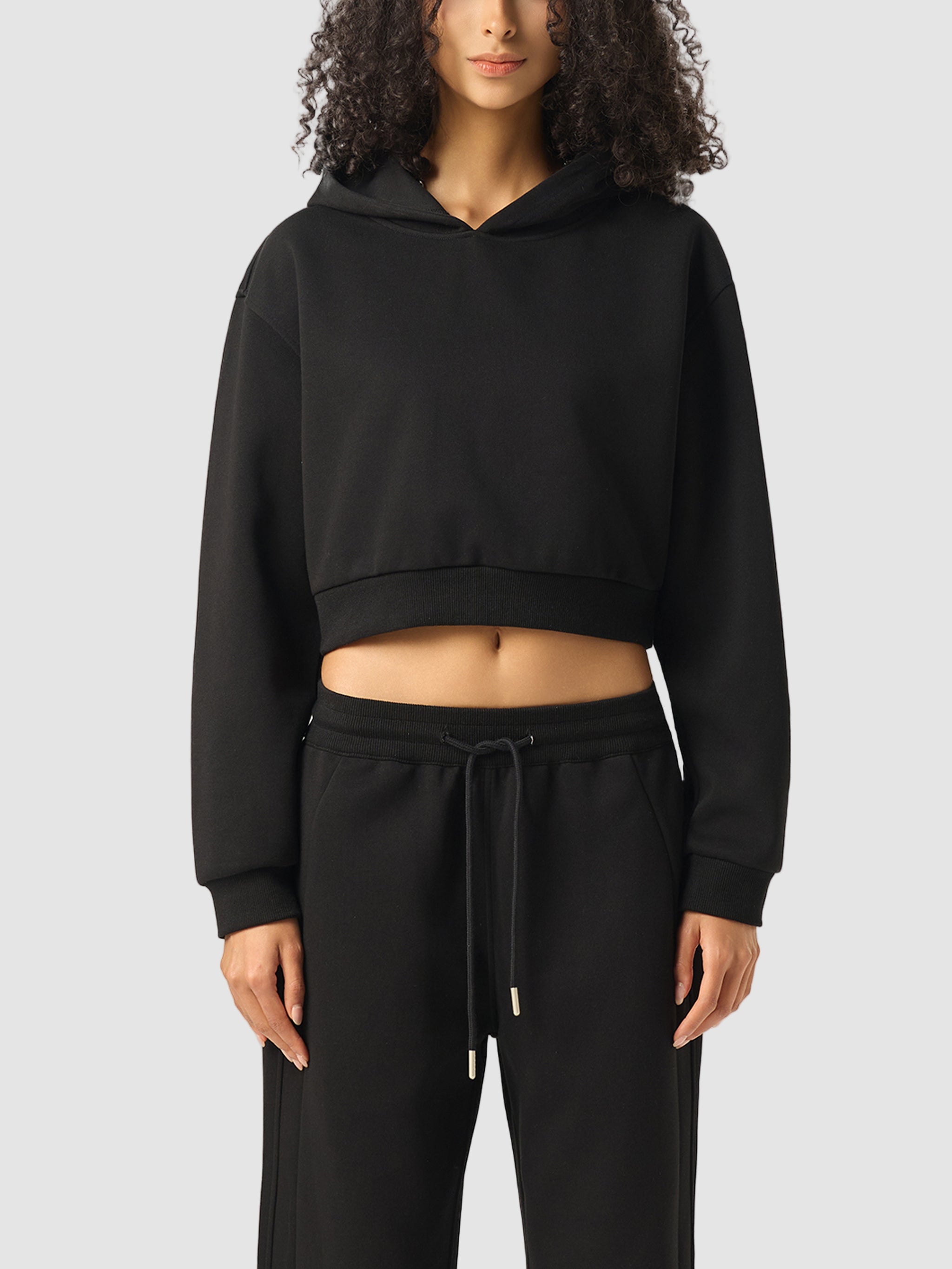 Person wearing a black cropped hoodie and black pants on a white background