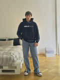 Person wearing a navy hoodie with 'VELVENIA' logo standing in a room with a bed and wooden floor.