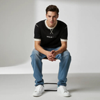 Man sitting on a white box wearing a black t-shirt with a brand logo, blue jeans, and white sneakers.