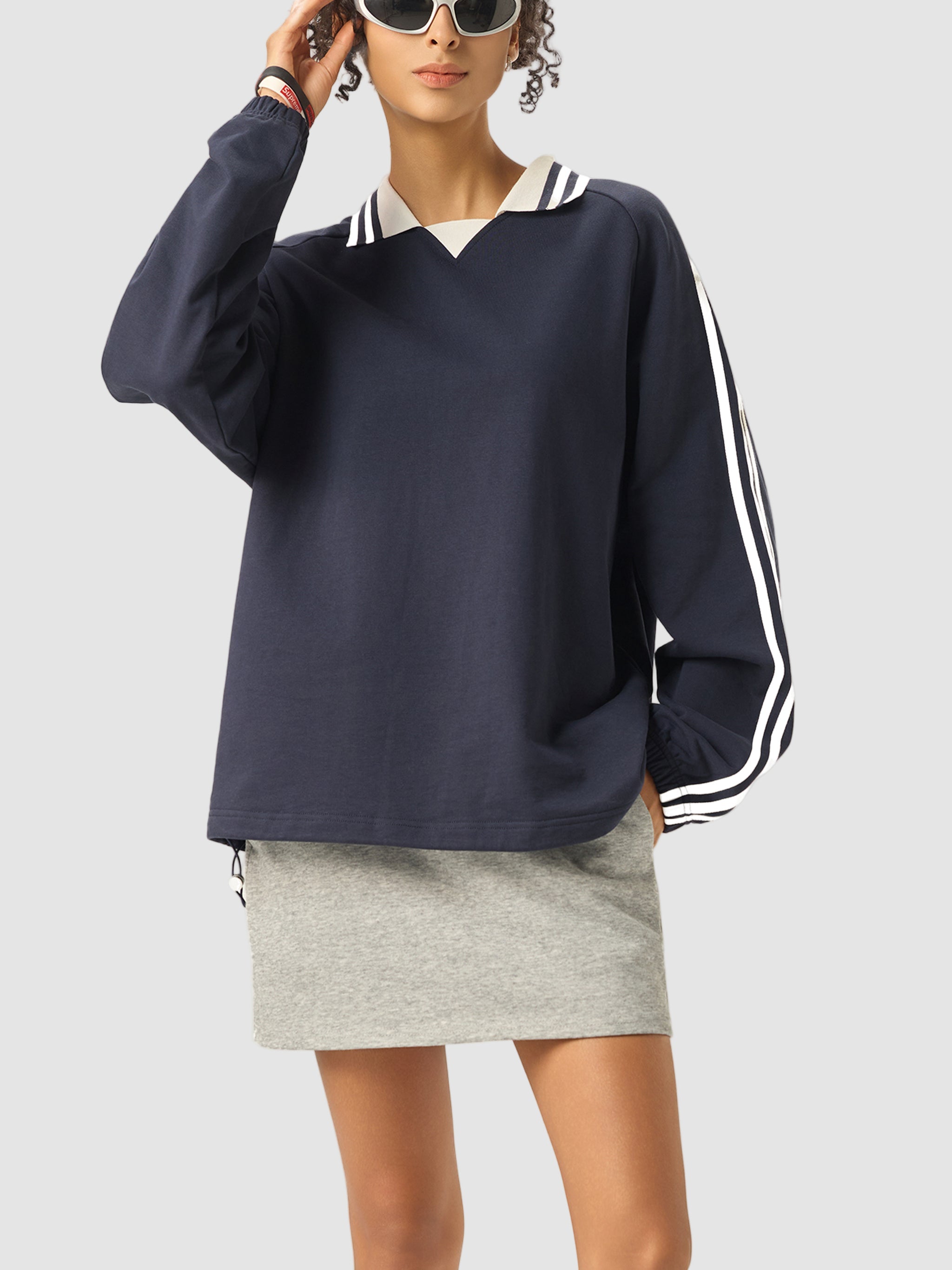 Person wearing a navy sweatshirt with white stripes and a gray skirt on a white background