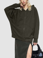 Person wearing a dark green hoodie with a zipper, holding a black handbag on a white background