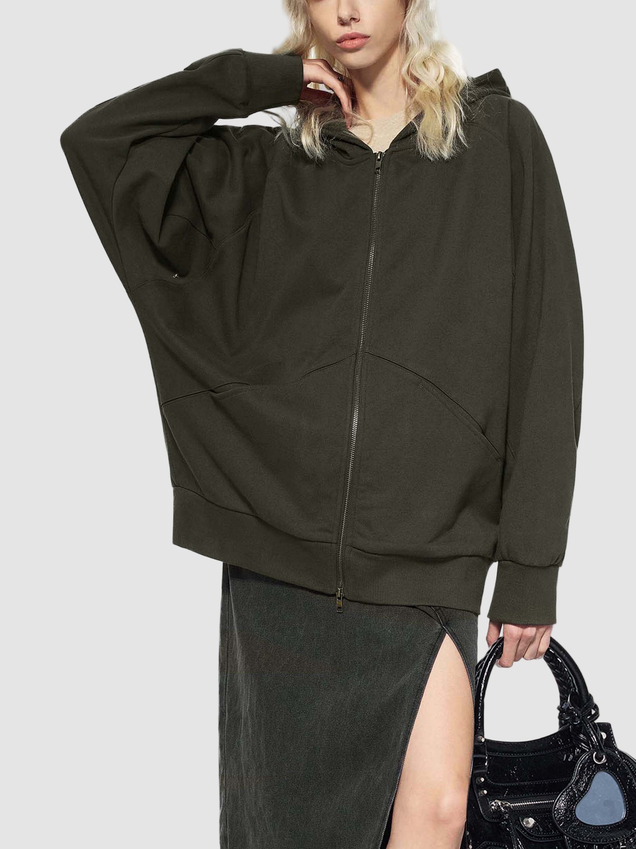 Person wearing a dark green hoodie with a zipper, holding a black handbag on a white background