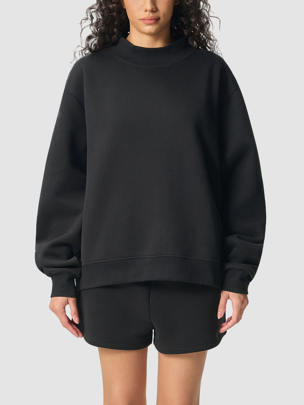 Person wearing a black sweatshirt and shorts on a white background