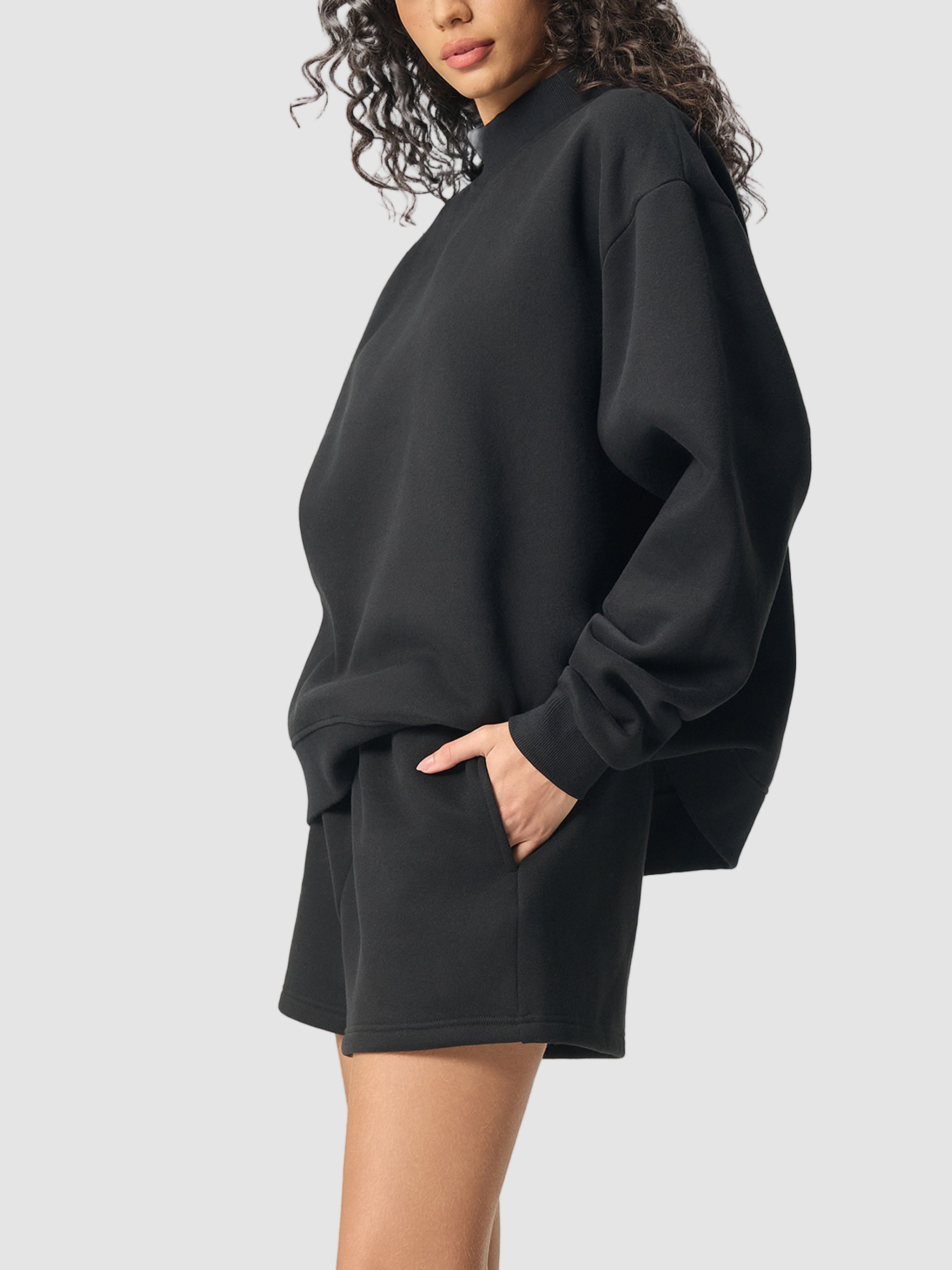 Person wearing a black oversized sweatshirt and shorts set on a white background