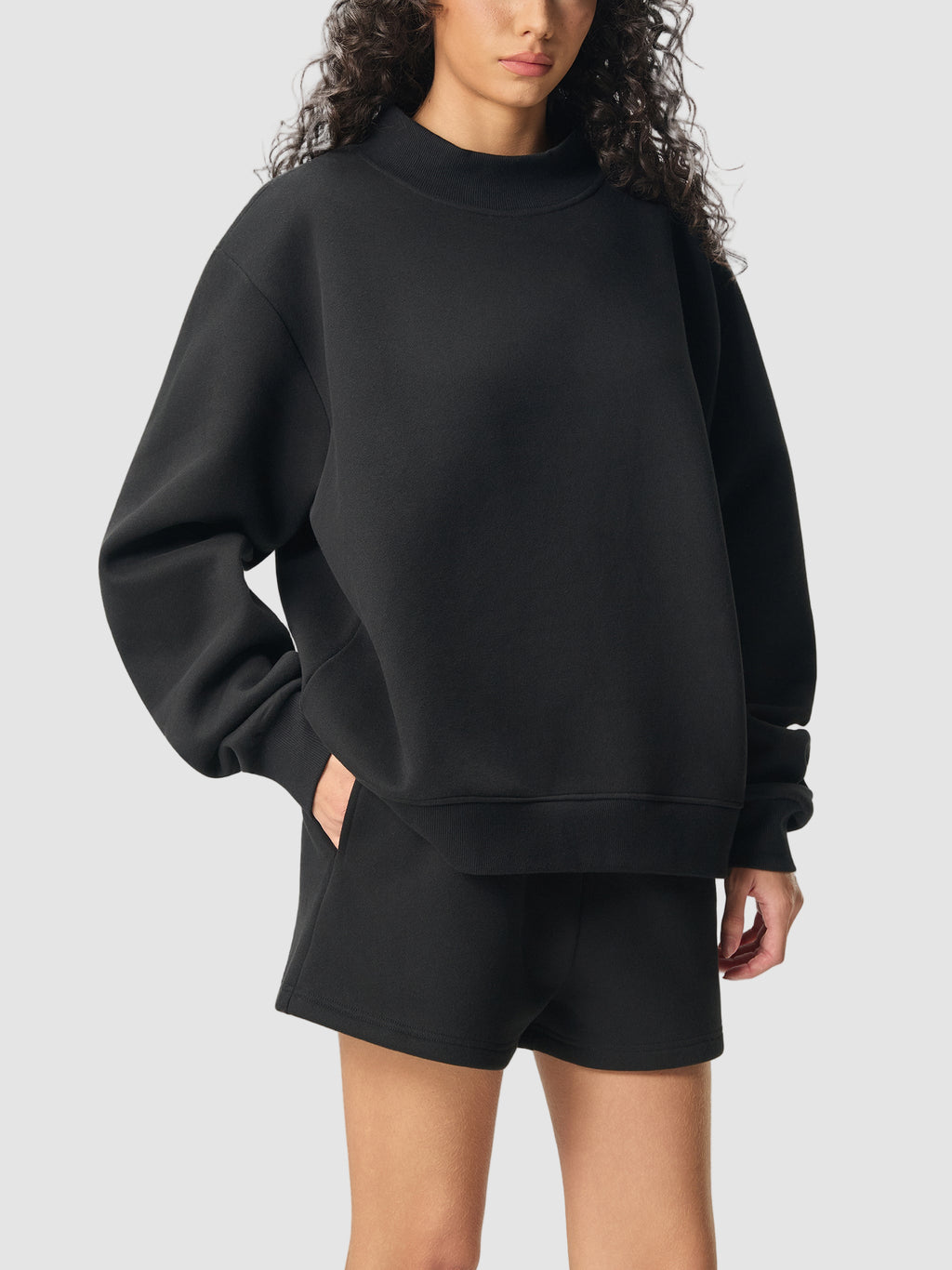 Person wearing a black sweatshirt and shorts on a white background
