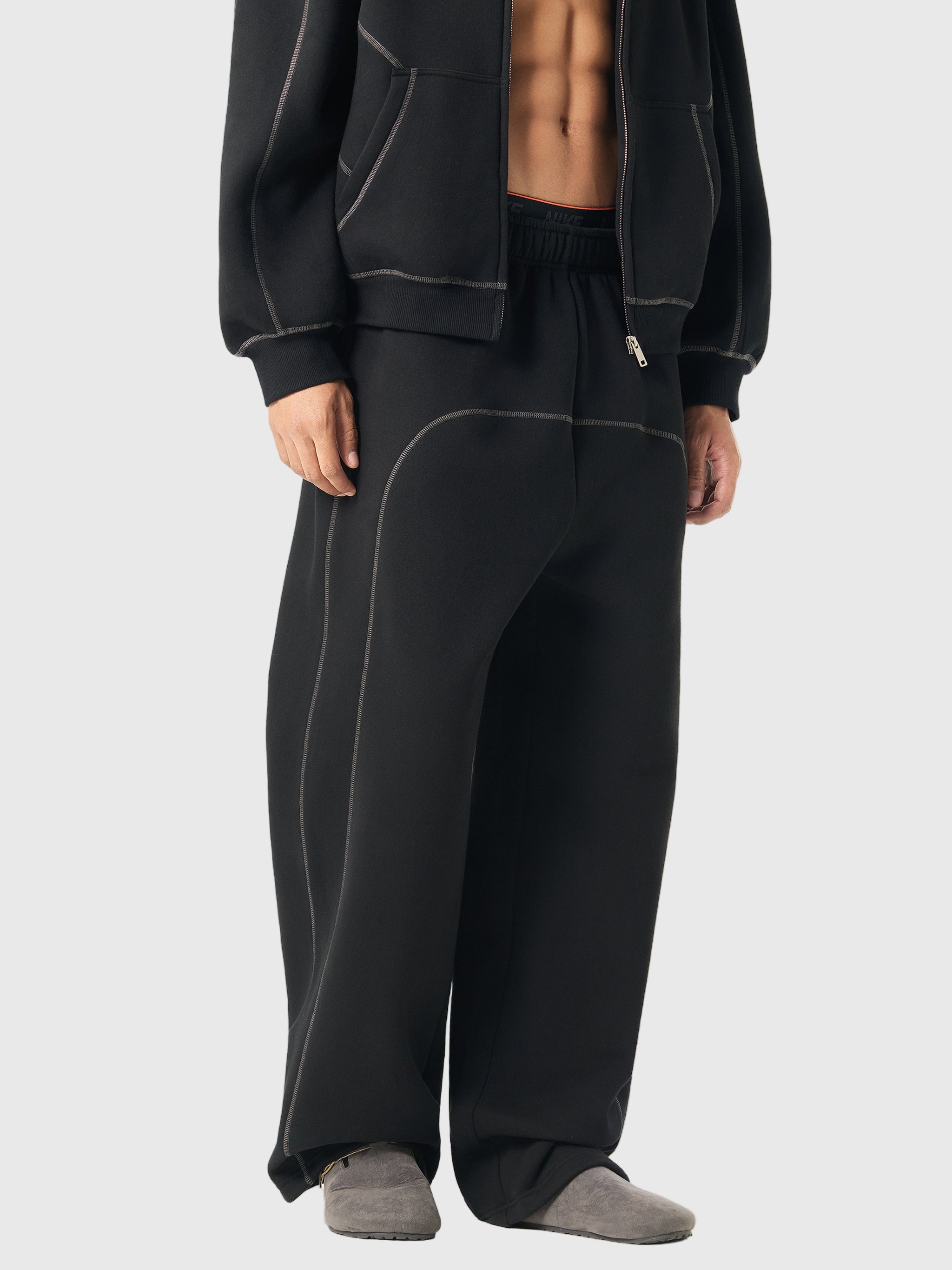 Person wearing black tracksuit pants and jacket on a white background