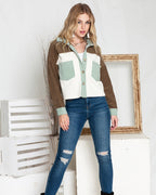 Woman wearing a brown and white jacket, light green shirt, blue jeans, and black boots in a minimalistic setting.